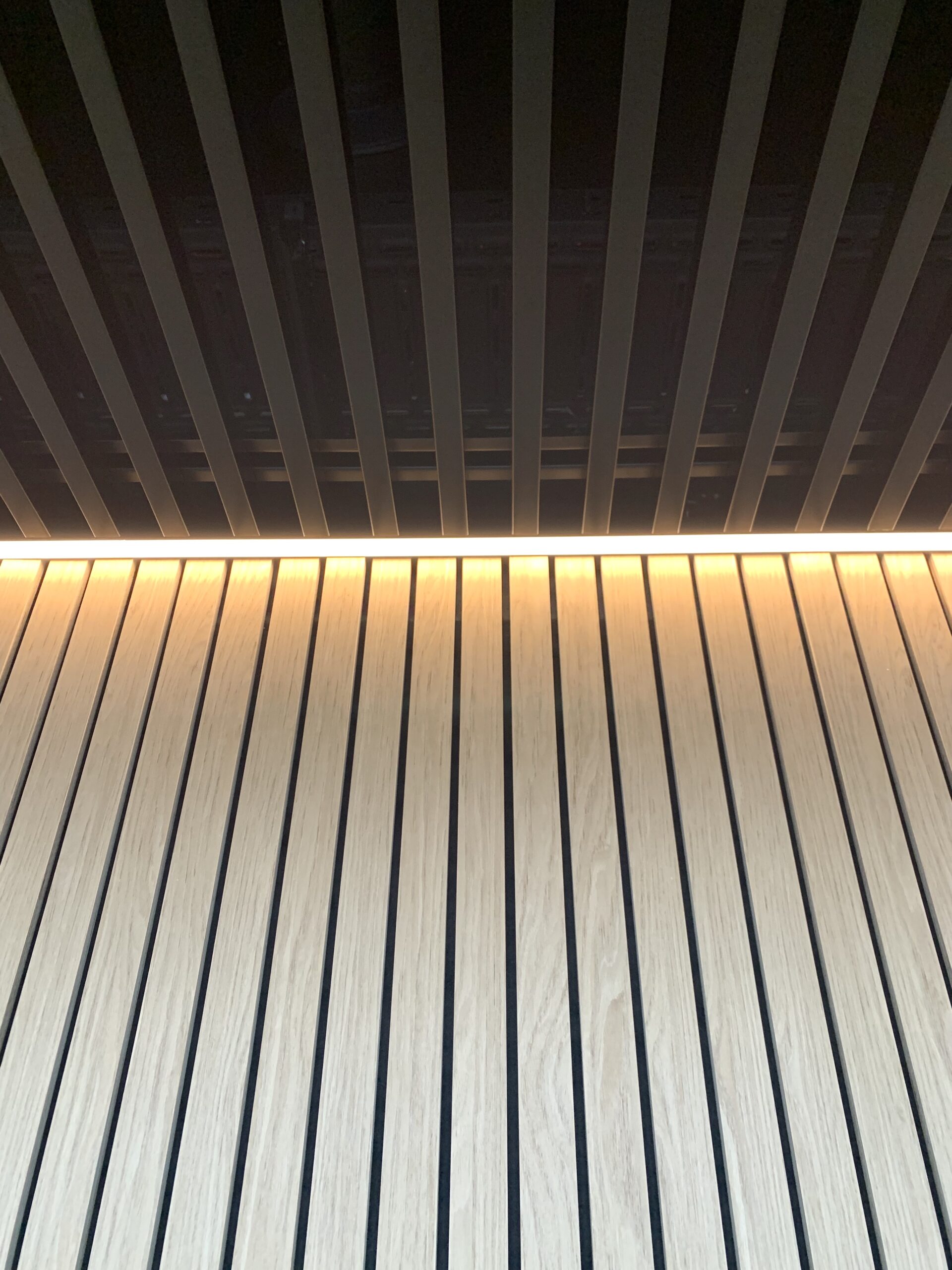 Detaljebillede af væg med trælameller og lys langs loftet